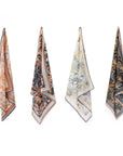 Four folded silk cotton scarves in earth tones displaying botanical and animal patterns in tan, cream, black and gold. Illustrated by Lisel Ashlock.