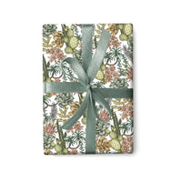 Desert botanical patterned gift wrap with cacti, succulents, and flowers tied with a green ribbon. Illustrated by Lisel Ashlock.
