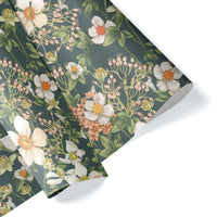 Rolls of floral gift wrap featuring white anemones and pink flowers on a deep teal background. Illustrated by Lisel Ashlock.