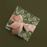 Gift wrapped box with white floral snowbells pattern on dark green background, tied with pink ribbon bow. Illustrated by Lisel Ashlock.