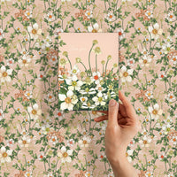 A hand holds a greeting card with white anemones against a floral patterned background, "Love you" text visible. Illustrated by Lisel Ashlock.