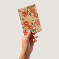 Hand holding a floral birthday greeting card with red and orange cosmos flowers on kraft paper. Illustrated by Lisel Ashlock.