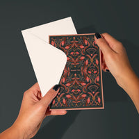 Hands holding open a red and dark filigree patterned thank you greeting card with blank white interior. Illustrated by Lisel Ashlock.
