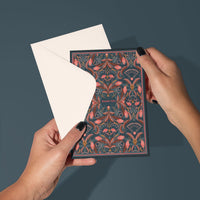 Hands holding an open blue and red filigree greeting card with "Thank You" text visible. Illustrated by Lisel Ashlock.