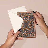 Hands holding open a "Thank You" greeting card with sea peach filigree pattern, revealing blank interior. Illustrated by Lisel Ashlock.