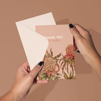 Hand holding a thank you greeting card with protea flower illustrations on a beige background. Illustrated by Lisel Ashlock.
