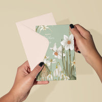Hands holding a Mother's Day greeting card with white flowers on sage green background and matching envelope. Illustrated by Lisel Ashlock.