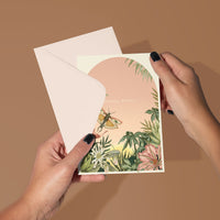A hand holding an open birthday greeting card with botanical illustrations and "Birthday Wishes" text. Illustrated by Lisel Ashlock.