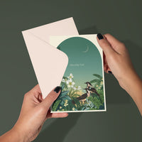 Hands holding a "Missing You" greeting card featuring a nighttime garden scene with birds and flowers. Illustrated by Lisel Ashlock.