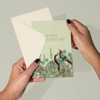 Hands holding a green "Happy Anniversary" greeting card with garden birds and flowers illustration by Lisel Ashlock.