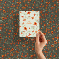 Hand holding a birthday greeting card with orange flowers on cream background against matching patterned wallpaper. Illustrated by Lisel Ashlock.