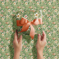 Hands holding wrapped gift with coral ribbon on green floral Anemone gift wrap. Illustrated by Lisel Ashlock.