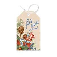 A "For you" gift tag featuring a red Dala horse with pinecones and greenery on cream cardstock. Illustrated by Lisel Ashlock.