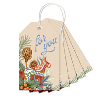 A stack of gift tags with "for you" text, a decorated red Dala horse, pineapples, and botanical elements. Illustrated by Lisel Ashlock.