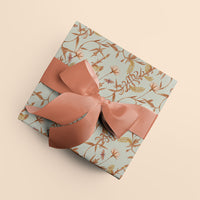 A wrapped gift with light blue botanical wrapping paper featuring rust-colored branches and leaves, tied with coral grosgrain ribbon bows. Illustrated by Lisel Ashlock.