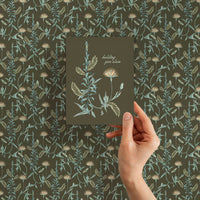 Hand holding gift wrap featuring botanical lily tree pattern in sage green and cream colors. Illustrated by Lisel Ashlock.