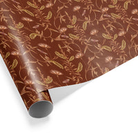 A rolled gift wrap featuring an ornate botanical pattern with golden ferns and delicate flowers on a rustic brown background. Illustrated by Lisel Ashlock.