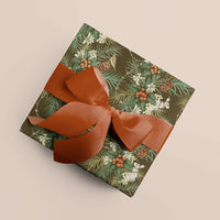 Two rolls of "Holly & Hare in Moss" gift wrap featuring woodland botanicals tied with a burnt orange ribbon on beige background. Illustrated by Lisel Ashlock.