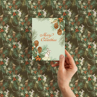 Hand holding a "Merry Christmas" card against Holly & Hare in Moss gift wrap. Illustrated by Lisel Ashlock.