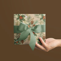 A hand holding a square gift wrapped in botanical holly and hare patterned paper with a sage green ribbon bow. Illustrated by Lisel Ashlock.