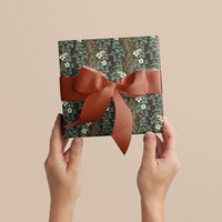 Two hands holding a wrapped gift with dark floral patterned paper and a rust-colored ribbon bow. Illustrated by Lisel Ashlock.