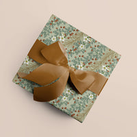 Wrapped gift with sage green botanical print wrapping paper featuring berries and white flowers, tied with a bronze ribbon bow. Illustrated by Lisel Ashlock.
