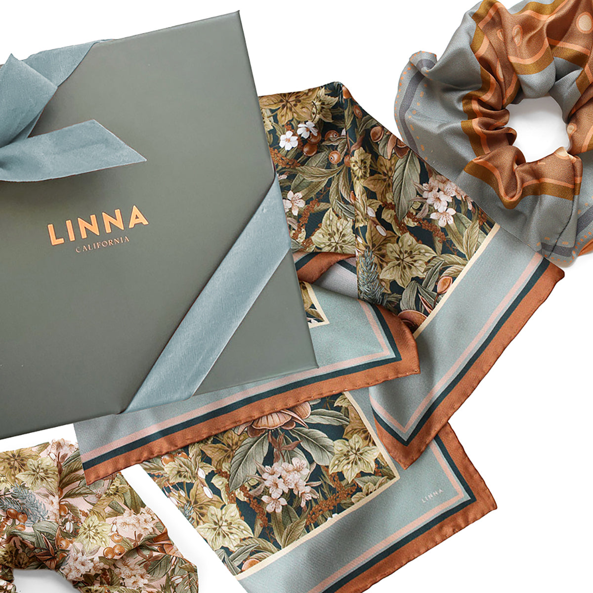 Linna California silk twill scarf with floral pattern, displayed with packaging and coordinating scrunchie. Illustrated by Lisel Ashlock.