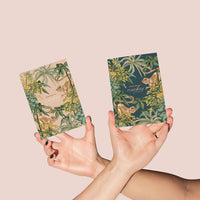 Two hands holding greeting cards with tropical monkey and floral design in pink and teal. Illustrated by Lisel Ashlock.