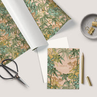 Flat lay of greeting card with botanical monkey pattern, envelope, scissors, pen, and desk accessories. Illustrated by Lisel Ashlock.