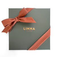 A sage green gift box with a coral silk twill scarf tied as a bow, featuring gold "LINNA CALIFORNIA" text.