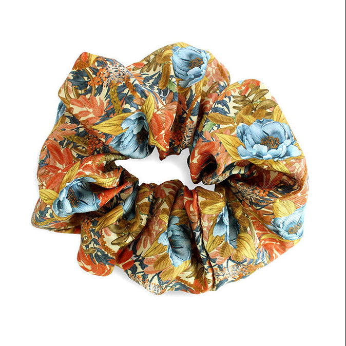 Colorful silk scrunchie with orange marigold flowers, blue blooms, and gold leaves pattern. Illustrated by Lisel Ashlock.