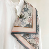 Angelite silk cotton scarf with botanical and butterfly print in cream, pink, and charcoal draped over white shirt. Illustrated by Lisel Ashlock.