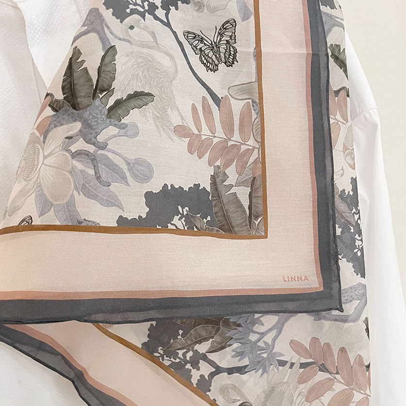 Folded silk cotton scarf featuring botanical illustration with leaves, flowers, and butterfly in muted tones. Illustrated by Lisel Ashlock.