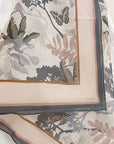 Folded silk cotton scarf featuring botanical illustration with leaves, flowers, and butterfly in muted tones. Illustrated by Lisel Ashlock.