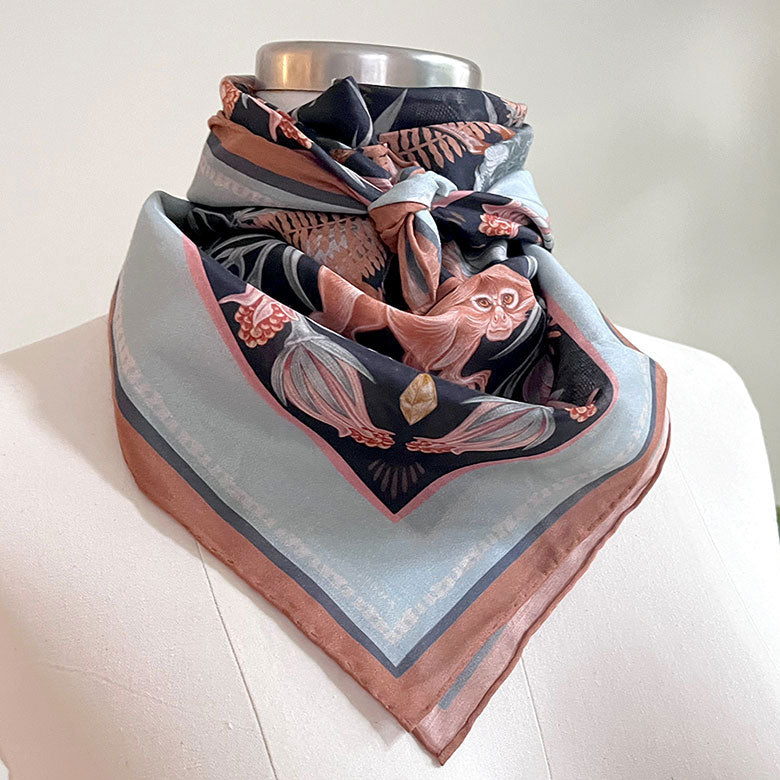 Silk cotton scarf in moonstone featuring illustrated bats, moths, and botanical elements in rust and black. Illustrated by Lisel Ashlock.