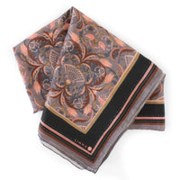 A folded silk cotton scarf in dusted lavender with ornate filigree floral design and black border stripe. Illustrated by Lisel Ashlock.