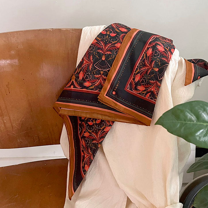 Bright Mahogany Filigree silk cotton scarf draped over a brown leather chair with cream fabric. Illustrated by Lisel Ashlock.