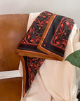 Bright Mahogany Filigree silk cotton scarf draped over a brown leather chair with cream fabric. Illustrated by Lisel Ashlock.