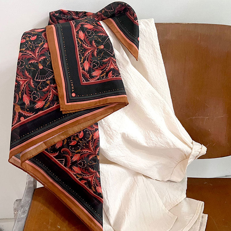 Silk cotton scarf with bright mahogany filigree pattern draped over wooden chair. Illustrated by Lisel Ashlock.