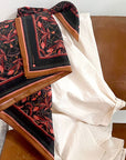 Silk cotton scarf with bright mahogany filigree pattern draped over wooden chair. Illustrated by Lisel Ashlock.