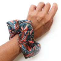 Person wearing a blue silk scrunchie with red rose pattern on their wrist. Illustrated by Lisel Ashlock.