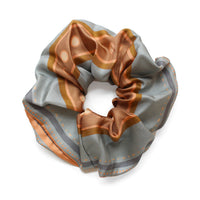 Apricot and gray striped silk scrunchie gathered in a circular shape against a white background, illustrated by Lisel Ashlock.