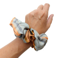 Hand wearing an apricot and gray striped silk scrunchie on the wrist. Illustrated by Lisel Ashlock.