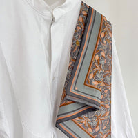 A white button-up shirt styled with an apricot filigree silk cotton scarf featuring orange and gray stripes. Illustrated by Lisel Ashlock.