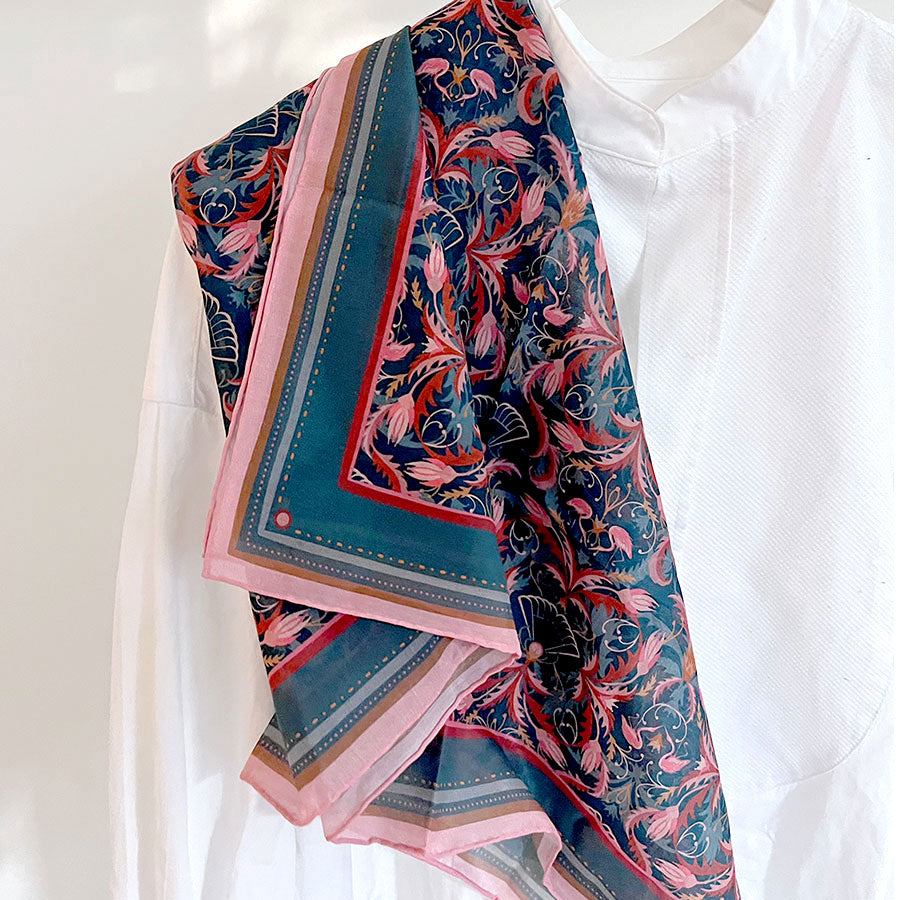 Colorful silk cotton scarf with blue rose filigree pattern draped on white mannequin. Illustrated by Lisel Ashlock.