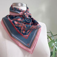 Blue rose filigree silk cotton scarf with pink border tied around mannequin neck. Illustrated by Lisel Ashlock.