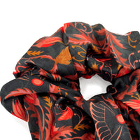 Bright mahogany silk scrunchie with red, orange, and black floral pattern bunched together. Illustrated by Lisel Ashlock.