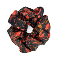 Bright Mahogany silk scrunchie with red and orange floral pattern on black background. Illustrated by Lisel Ashlock.