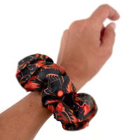 Person wearing a bright mahogany patterned silk scrunchie on their wrist. Illustrated by Lisel Ashlock.