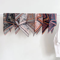 Multiple silk cotton scarves with floral and geometric patterns in apricot, navy, and blush tones displayed on a rod. Illustrated by Lisel Ashlock.